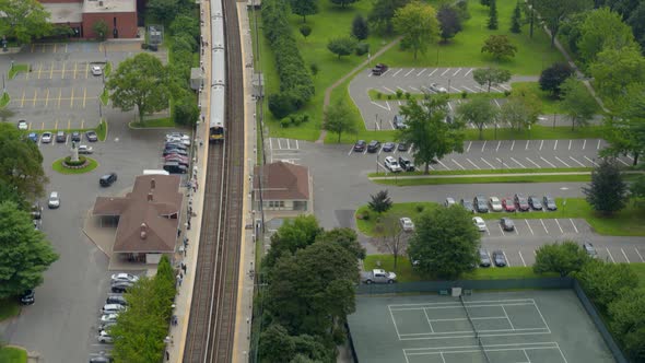 Tilt Down Aerial of Train Arriving at Station Near Tennis Courts in Long Island alt