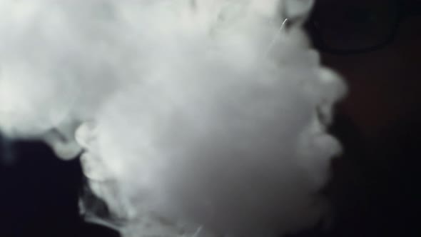 Young Bearded Man in Glasses Smokes a Hookah and Blow Out Smoke Closeup on Black Background in Slow