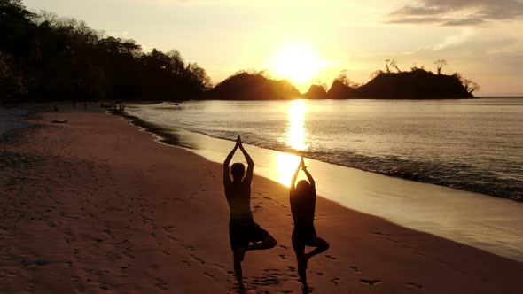 Young Couple Practicing Yoga on the Beach at Sunset
