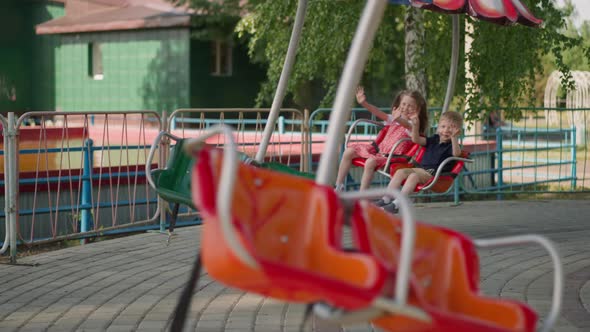 Happy Little Children Wave Hands Riding Carousel in Park alt