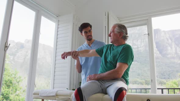 Slow motion shot of male physiotherapist helping senior patient exercising at retirement home alt