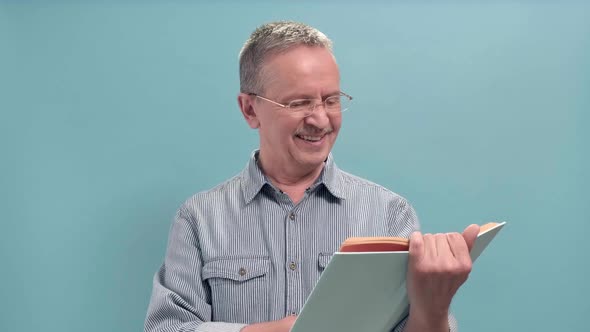 Aged Man with Blue Shirt Holds Open Book in Her Hands on a Blue Background alt