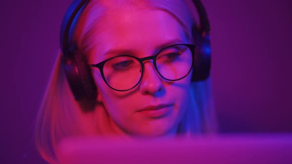 A Cute Woman with Beautiful Eyes in Headphones Sits at a Computer in Neon Light