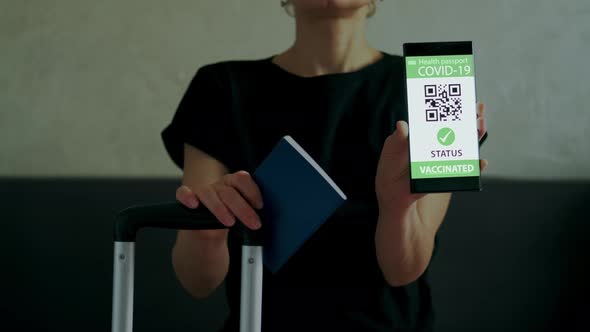 Woman Demonstrates Smartphone with Vaccination Passport Allowing Travel in Suitcase alt