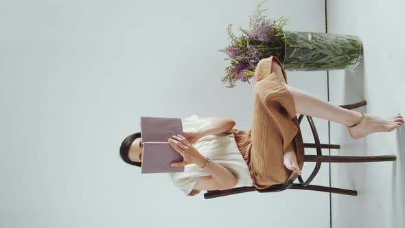 Barefoot Woman Reading Book in Studio with Flowers in Vase alt