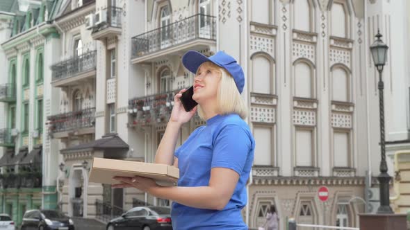 Female Courier Calling a Client Delivering Pizza in the City