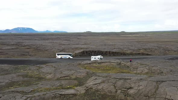Recreational Vehicle and a tour bus located in lava field in Iceland with drone video moving forward alt