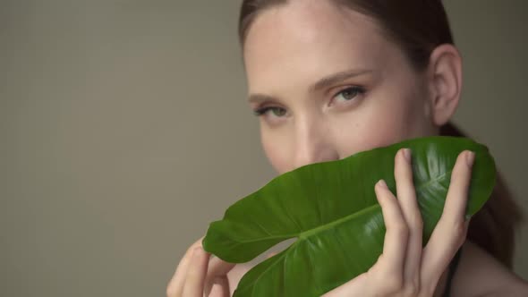 Beautiful young woman with soft and clean skin posing with tropical leaves.