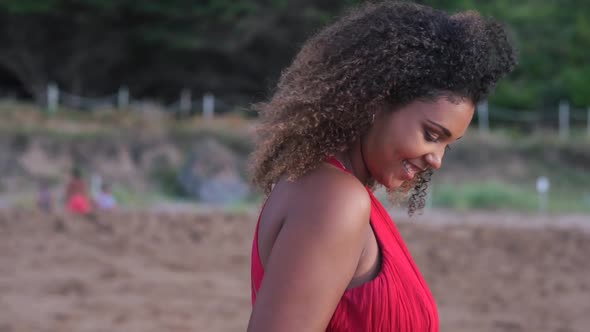 Smiling young woman standing on beach touching her curly hair alt