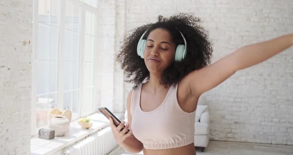 Young Trendy Woman in Big Headphones Listening Music and Dancing at Home alt
