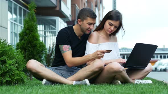 Happy Couple Makes Online Purchases Using the Laptop, Choose Goods and Enters a Credit Card Number alt