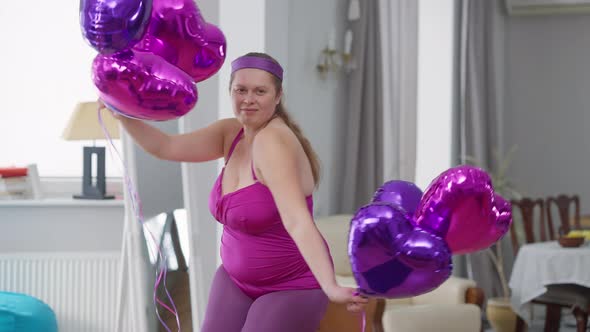 Cheerful Confident Plussize Woman Dancing with Balloons at Home Looking at Camera Smiling alt