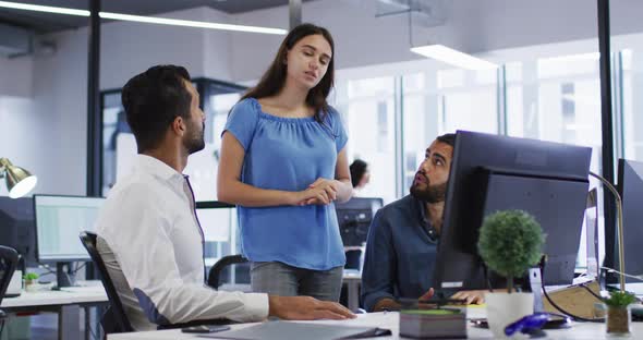 Caucasian businesswoman standing in discussion with two mixed race male colleagues at their desk alt