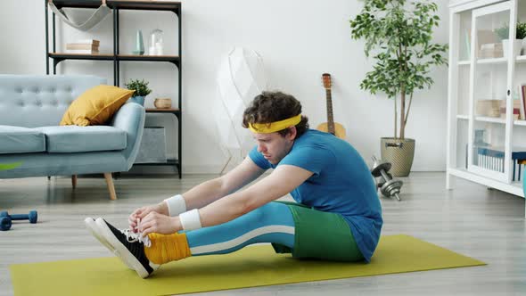 Awkward Guy in Bright Sports Outfit Stretching Body Then Tying Shoelaces Exercising on Yoga Mat at alt