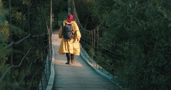 Man Hiking Dressed in Yellow Raincoat Walking on Suspension Bridge