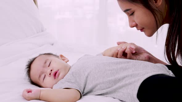 Asian young beautiful mother gently holds and kisses her newborn baby's hand