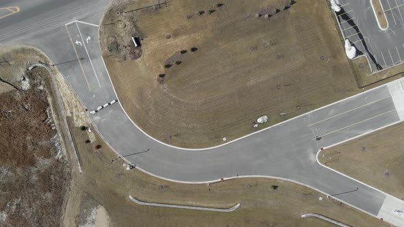 Top down view of exit from parking lot to highway. Lane lines present. Barricades to highway.