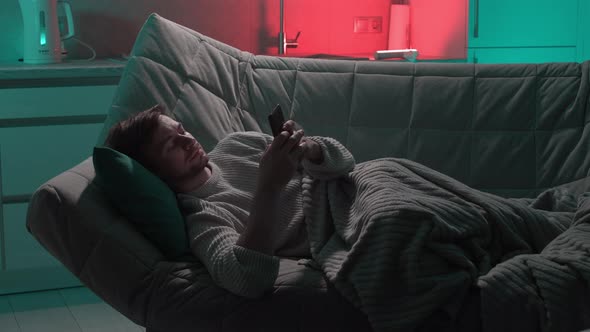 A Man Lying in Bed Uses a Smartphone