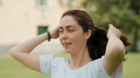 Portrait of a young smiling woman tying her hair in a ponytail. Real time. alt