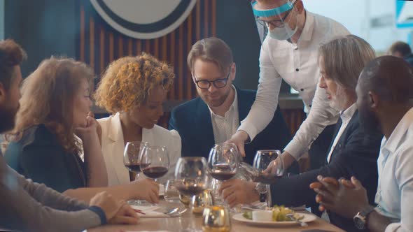 Waiter in Safety Mask Serving Delicious Dish for Customers in Modern Restaurant alt