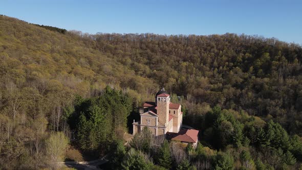 Moving away from church built in the forest on the side of a mountain on clear blue day.