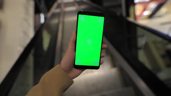 POV, Female Hand Holding Smartphone Green Screen in a Mall Escalator
