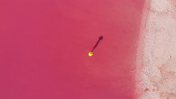 Aerial Drone View Surreal View of Pink Lake and Girl with Yellow Umbrella alt