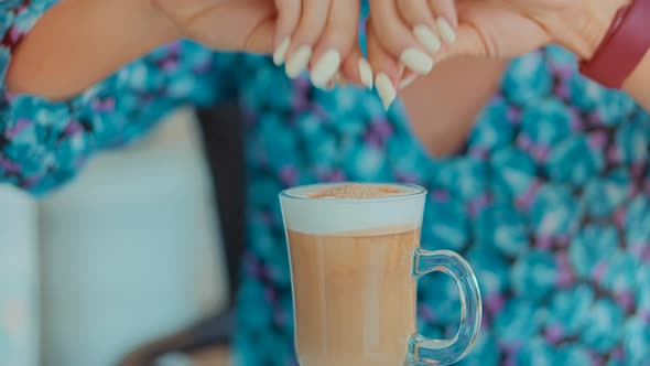 Woman Drinking Cappuccino In Cafe .Girl Having Breakfast In Cafeteria. Adding Sugar In Latte Coffe alt
