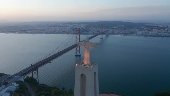 Aerial Evening Back View of Big Jesus Statue on Pedestal and Long Bridge Over River alt