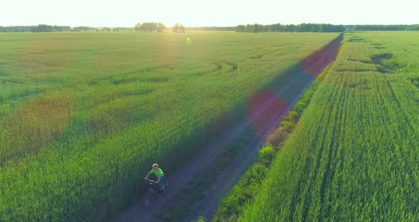 Aerial View on Young Boy That Rides a Bicycle Thru a Wheat Grass Field on the Old Rural Road alt