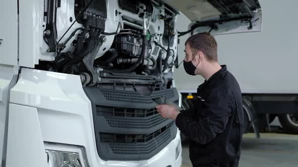 engineer in protective mask stands in repair shop using modern device tablet alt