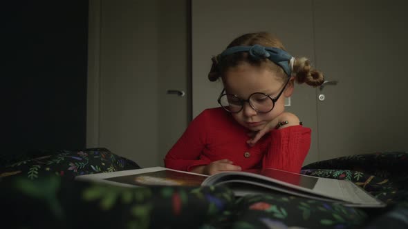 Little Girl in Glasses Lying on the Bed and Reading Book alt