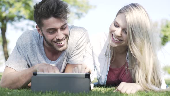 Couple using digital tablet in park alt