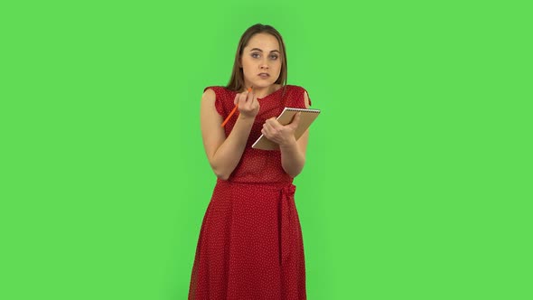 Tender Girl in Red Dress Is Angrily Writing with Pencil in Notebook. Green Screen alt