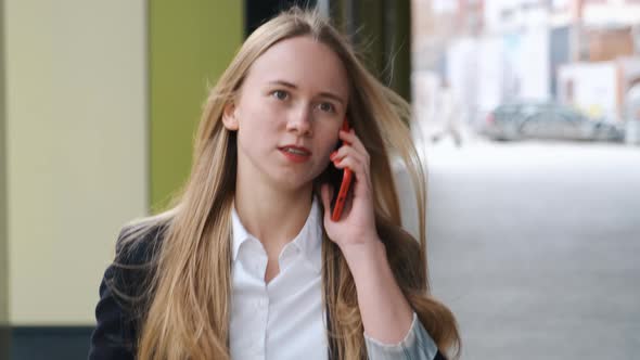 Attractive Blond Student Girl is Talking By Phone While Walking Near University