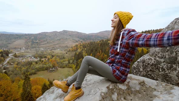 POV First Person View of Woman Hiker in Warm Casual Wear Sits on Edge of Cliff Against Background of alt