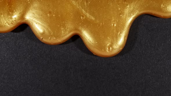 Golden Liquid Gel with Micro Bubbles As It Slowly Slides Down on the Black Surface alt