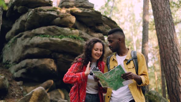 Happy Brunette with Curly Hair Is Looking Through Binoculars Standing in Forest Near Rocks While Her alt