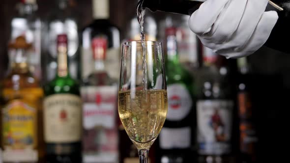 Closeup of a Bartender in White Gloves Pouring Champagne Into a Glass in a Bar alt