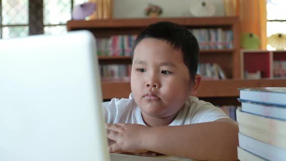 Little asian boy studying online from home watching web class lesson or listening tutor