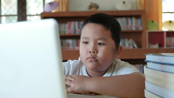 Little asian boy studying online from home watching web class lesson or listening tutor alt