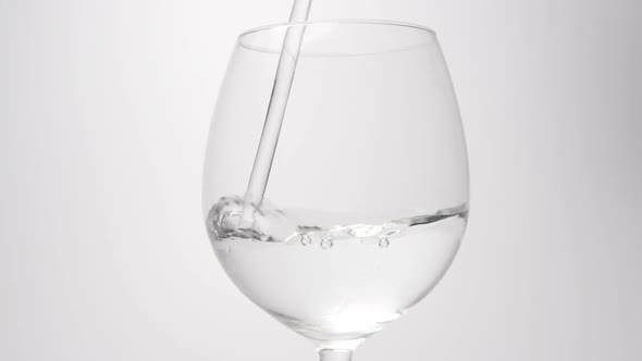 Water stream falls into a wine glass on a white background