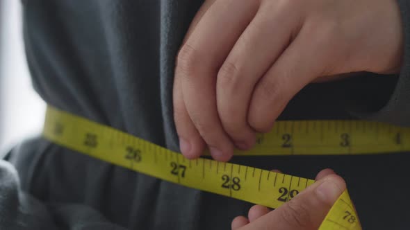 Close up Asian woman measuring her waist-length with tape while standing in the living room.