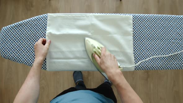 Young Adult Man Ironing A White Pillowcase On An Ironing Board At Home alt