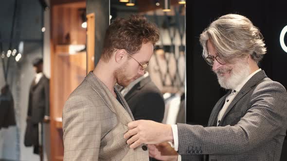 Man Trying Business Suit on with Consultant at Men Clothing Store alt