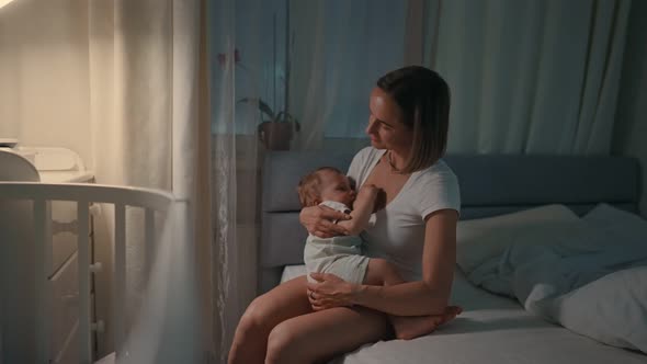 Young Beautiful Mother Breastfeeding Her Newborn Baby Boy at Night Dim Light alt