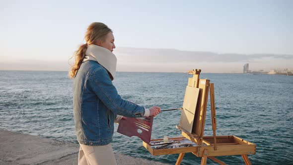Young Inspired Woman Artist Painting Cityview Picture on River Bank with Portable Easel Tracking alt