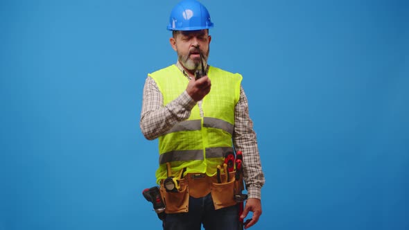 Senior Man Builder Using Walkietalkie Against Blue Background in Studio
