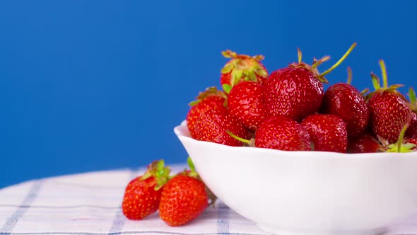 Ripe Strawberries Rotate on a Blue Background in a White Plate