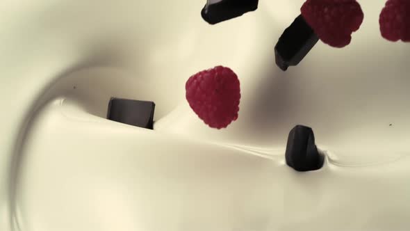 Raspberries and chocolate pieces fall down into pouring creamy milk in slow motion